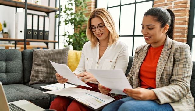 Two Colleagues Collaborating and Reviewing Documents on Sofa in Modern Office Lounge