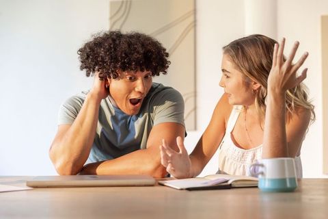 Sunlit kitchen surprise: young couple reacting to laptop news while discussing plans