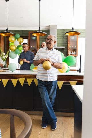 Senior men decorating kitchen with gold and green balloons for home celebration