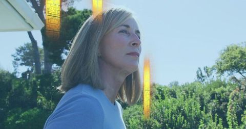 Gazing mature woman contemplating in sunlit suburban garden with golden light flares