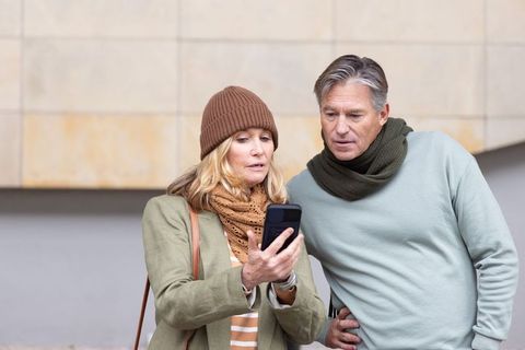 Senior couple studying smartphone on urban sidewalk, leaning in, casual autumn attire