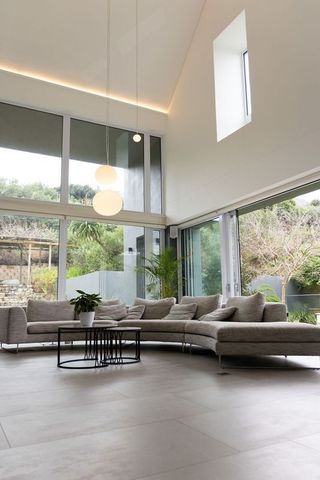 Sunlit minimalist living room featuring curved gray sectional and floor-to-ceiling windows