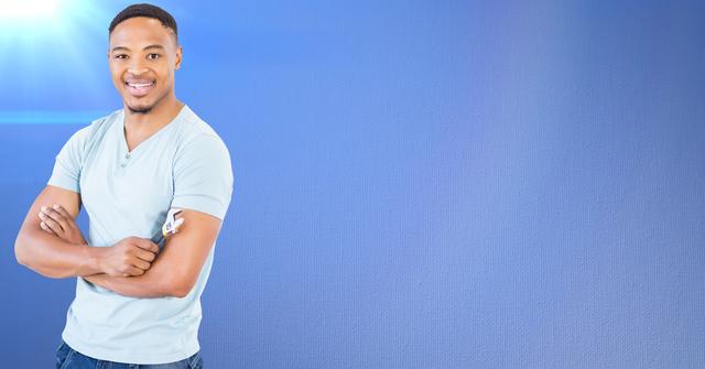 This image features a confident, smiling man with his arms crossed, standing against a solid blue background. He is casually dressed in a light-colored shirt and jeans, conveying a relaxed and positive attitude. This image can be used in various contexts such as advertisements, marketing materials, websites, or promotional content where themes of confidence, positivity, and casual fashion are relevant.