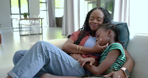 African mother cradling sleeping daughter on sofa, tender maternal bonding at home