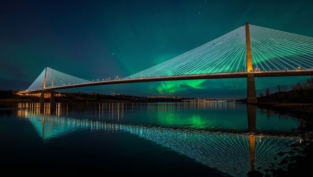 Illuminated cable-stayed bridge reflecting aurora borealis over mirrorlike river nightscape