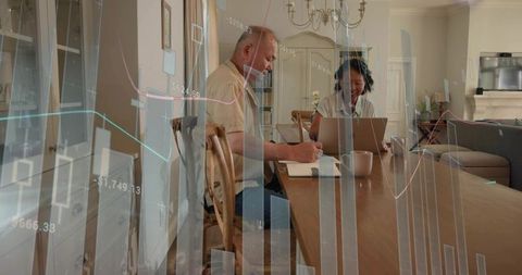 Mature couple working remotely at home using laptop taking notes and reviewing finances
