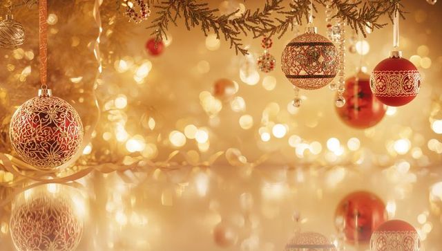 Hanging golden bokeh Christmas ornaments glowing on evergreen with red filigree baubles