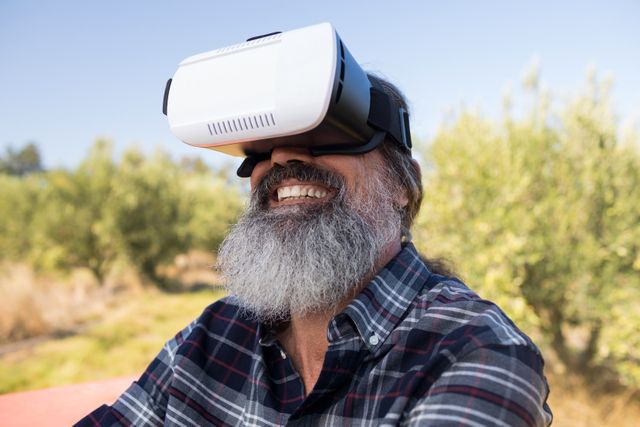 Happy man using virtual reality headset in olive farm on a sunny day