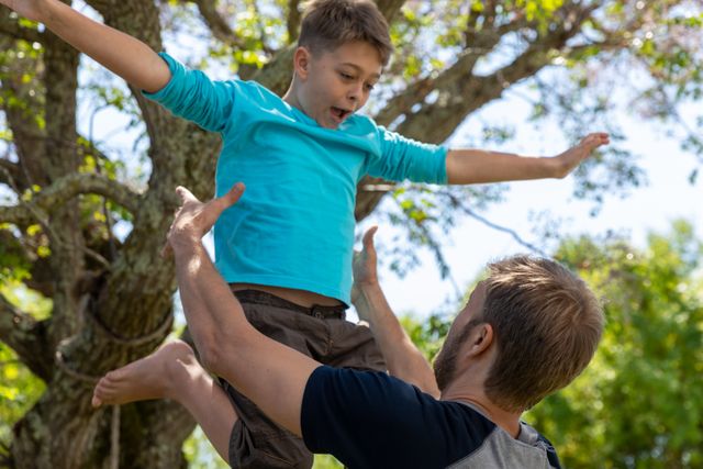 Caucasian dad having fun with his son in their backyard. the dad is throwing his son up in the air.