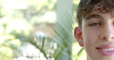 Smiling teen male half-face portrait on shaded veranda with palm frond and sunlit bokeh