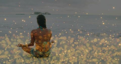 Golden bokeh meditation on quiet beach facing overcast sea woman sitting meditating