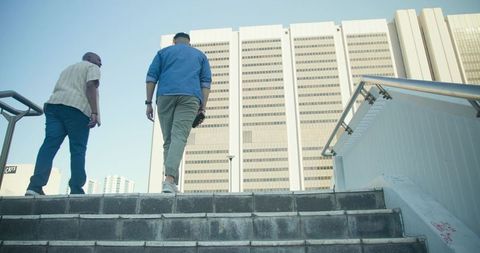 Two men walking up concrete stairs toward modern office tower low-angle urban commuting