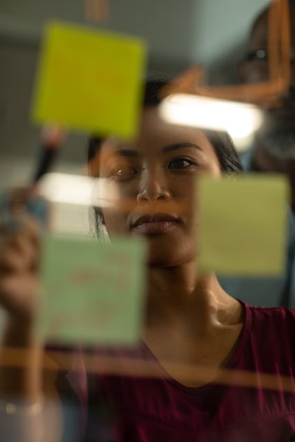 Close up of an Asian businesswoman working late in the evening in a modern office, writing on a glass moodboard. 
