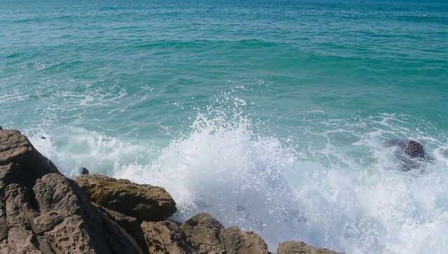 Crashing turquoise waves breaking against rugged coastal rocks with white spray