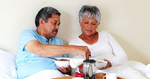 Middle Aged Hispanic Couple Relaxing in Bed with Breakfast