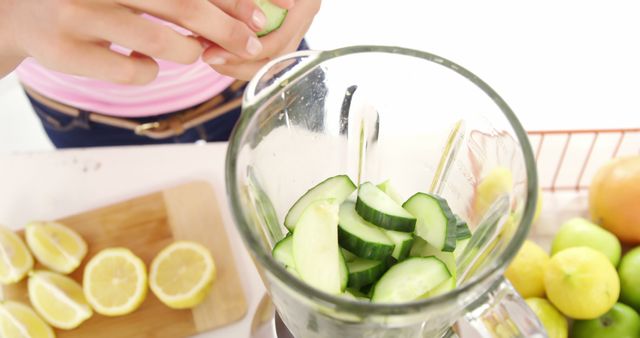Cucumber slices with lemon being put into a blender for fresh smoothie preparation. Perfect for healthy eating illustrations, recipe blogging, healthy food promotions, cooking at home themes, diet-focused content.