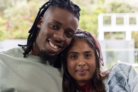 Smiling interracial couple leaning together on balcony with denim jacket and headscarf