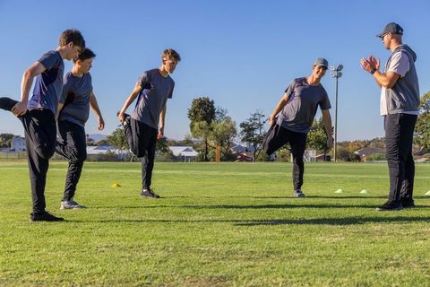 Male athletes stretching and balancing during outdoor team training session with coach