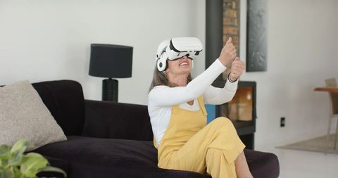 Senior woman enjoying virtual reality adventure at home wearing VR headset and headphones
