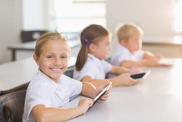 Schoolgirl smiling while using a digital tablet in a classroom with other students in the background. Ideal for educational content, technology in education, modern classroom settings, and academic materials.