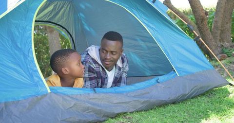 African american father and son camping in backyard tent sharing conversation on sunny lawn