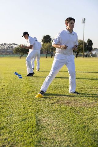 Male cricket players practicing lateral agility and footwork drills on sunlit grass field