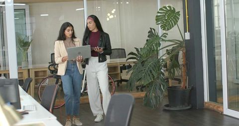 Two Professional Women Walking in Coworking Space Holding Laptop and Tablet Collaborating