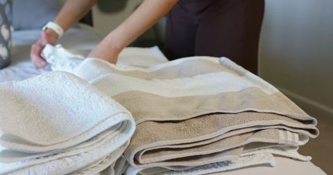 Folding and arranging neutral striped towels on bed for minimalist linen organization