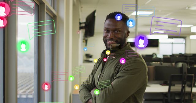 Image of profile and message icons over african american man with crossed arms smiling at office. Social media networking and business technology concept