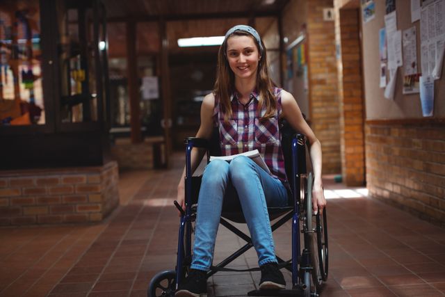 Portrait of smiling disabled schoolgirl on wheelchair in corridor at school