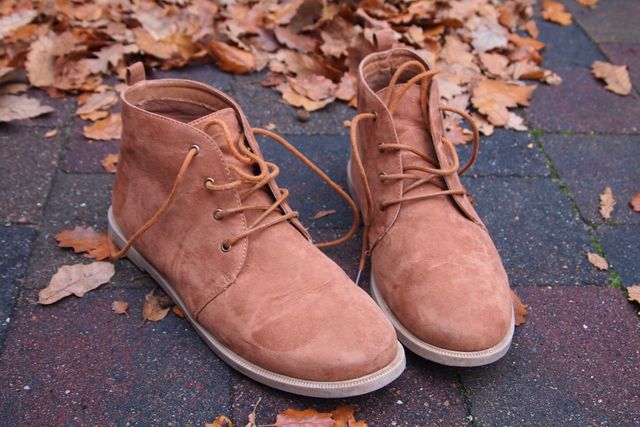 This image shows a pair of tan suede boots placed on a brick pavement surrounded by scattered autumn leaves. Ideal for promoting fall fashion collections, footwear brands, or seasonal outfit inspirations. Great for use in blogs, advertisements, and social media posts focusing on autumn and casual style.