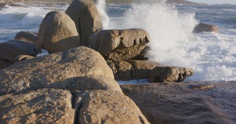 Waves Crashing on Granite Boulders at Rocky Shoreline in Sunlight