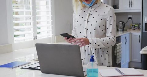 Woman Multitasking with Smartphone and Laptop in Modern Kitchen