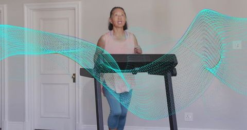 Senior woman walking on treadmill at home with turquoise digital wave overlay for fitness