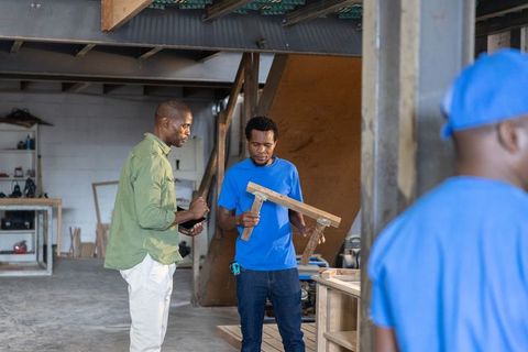 African american carpenters collaborating on wooden t-joint using tablet in workshop