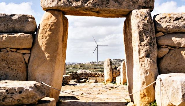 Ancient megalithic doorway framing modern wind turbine over limestone rural landscape