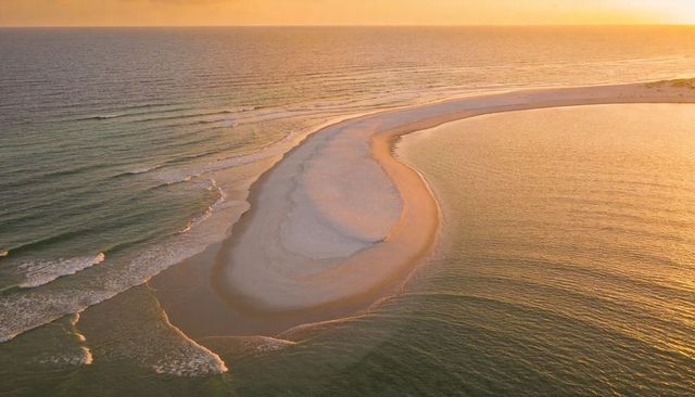 Golden sunset bathing curved sandbar and crescent lagoon over calm tidal waters
