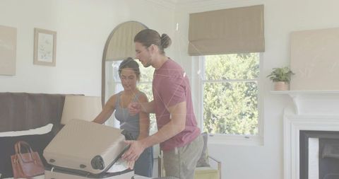 Young couple packing luggage in minimalist bedroom leaning over beige suitcase