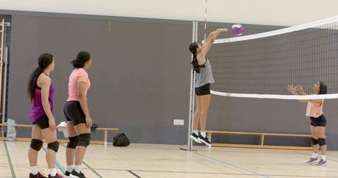 Diverse female volleyball team practicing net attack and blocking in indoor gym
