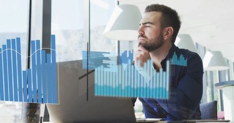 Business analyst studying financial charts on laptop in modern glass office with city view