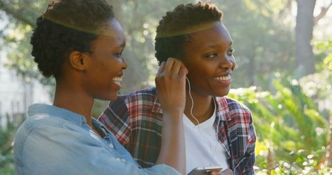 Smiling Twin Sisters Sharing Earphones in Sunny Park