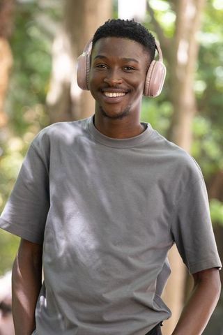 Young african man smiling and listening with pale pink headphones in sunlit park