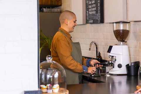 Smiling male barista preparing espresso with portafilter at modern cafe counter, pastries visible