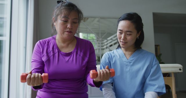 Asian female physiotherapist helping female patient exercise arms with dumbbells at surgery - Download Free Stock Photos Pikwizard.com