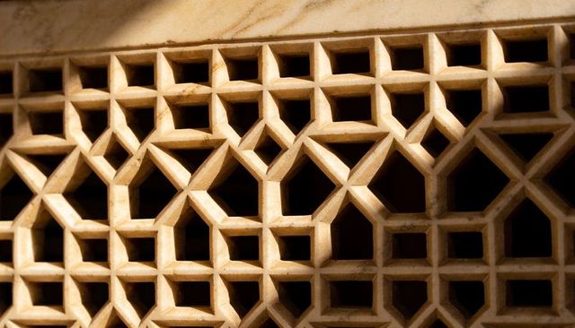 Sunlit carved sandstone jali lattice with geometric star pattern and deep shadow relief