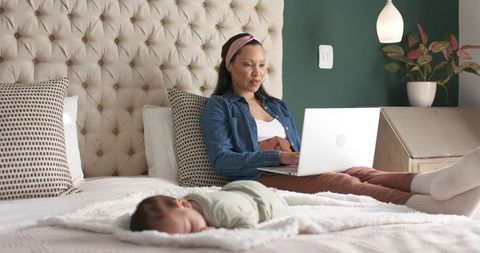 Working Mother on Bed Near Sleeping Infant in Comfortable Home Setting