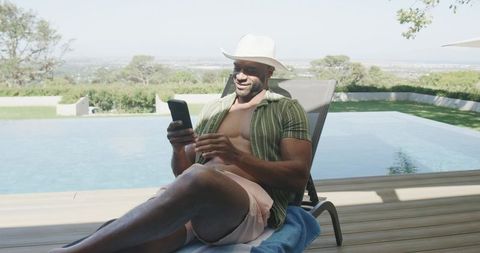 Relaxing poolside lounger with smartphone, sun hat and pink swim shorts for leisure