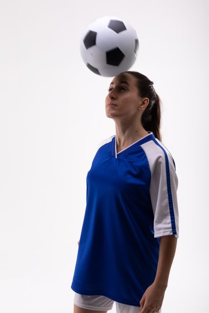 Young caucasian female soccer player in blue jersey and white shorts heading a soccer ball. Ideal for sports-related content, athletic training materials, soccer coaching guides, and promotional materials for women's sports events.