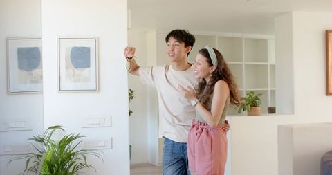 Young diverse couple celebrating new home holding keys while smiling in bright modern apartment