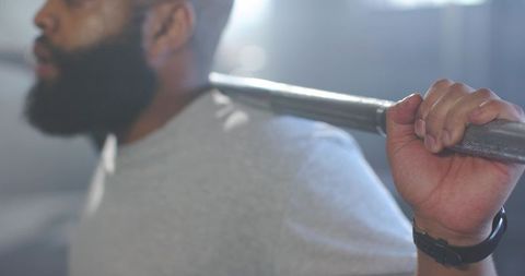 African man lifting barbell across shoulders backlit gym bokeh conveying strength and focus